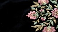 Elegant floral embroidery with pink flowers and golden leaves on black fabric showcasing traditional needlework craftsmanship for fashion and textile design.