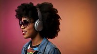 Young African American woman with curly afro hair wearing headphones and sunglasses in profile against colorful gradient background for music and lifestyle content.
