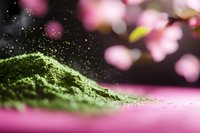 Green matcha tea powder with floating particles against soft pink bokeh background for culinary and wellness applications.