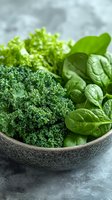 Fresh green leafy vegetables including kale, spinach and lettuce in ceramic bowl on gray stone background, healthy nutrition concept.