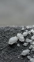 Clear quartz crystal specimens scattered on dark volcanic ash surface with soft gray background for healing and meditation practices.