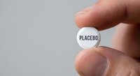 Hand holding white placebo pill between fingers against neutral background for medical research and pharmaceutical testing concepts.