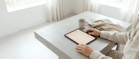 Caucasian woman in linen shirt using digital tablet with blank screen on minimalist concrete desk, natural light, cozy home office workspace.