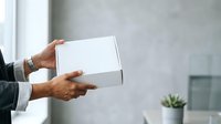 Man in business attire holding white cardboard box for delivery, shipping, or product packaging concepts in modern office setting.