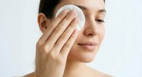 Young woman gently removing makeup with cotton pad during skincare routine, cleansing face with natural beauty treatment for healthy glowing skin.