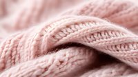 Soft pink knitted wool texture in macro view showing detailed yarn pattern and stitches. Natural fiber material background with gentle blurred effect.