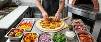Professional chef preparing fresh pizza with colorful toppings in commercial kitchen. Hands arranging vegetables on dough at pizza station with ingredients.