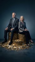 Senior Caucasian business executives sitting on pile of golden coins representing wealth, success and financial achievement in corporate environment.