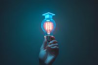 Glowing lightbulb with graduation cap icon floating above, held by hand against dark background, representing educational innovation and bright ideas.