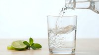 Fresh sparkling water being poured into glass with lime and mint garnish on wooden table against white background for healthy lifestyle concepts.