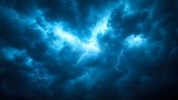 Dramatic lightning strike illuminates stormy night sky with electric blue glow through dark thunderclouds, creating atmospheric scene for weather and nature backgrounds.