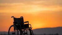 Silhouette of empty wheelchair against golden sunset sky with mountains in background, symbolizing hope, recovery, and accessibility for healthcare and rehabilitation concepts.