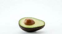 Fresh ripe avocado half with pit on white background isolated for healthy cooking and nutrition design projects.