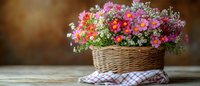 Vibrant pink and red flowers arranged in woven wicker basket on rustic wooden table with checkered cloth, creating cozy countryside atmosphere. Perfect for home decor.