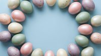Pastel Easter eggs arranged in a circle frame on a light blue background, creating a festive spring holiday flat lay with copy space.