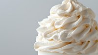 Swirled vanilla cream frosting in soft white peaks against light background, showcasing delicate texture and smooth piping technique for bakery and dessert designs.