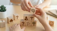 Hands arranging wooden blocks with healthcare and wellness symbols including medical caduceus, brain, and tree icons on desk.