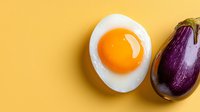 Fresh sunny side up egg and whole purple eggplant on vibrant yellow background with copy space. Minimalist food composition for healthy eating concept.