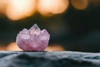 Purple amethyst crystal cluster on dark stone surface with warm bokeh lights background for meditation and healing practices.