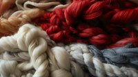 Soft twisted yarn skeins in red, white, gray and beige colors arranged in gentle folds creating textural composition, close-up view of natural wool fibers.