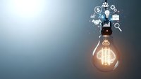 Glowing light bulb with business icons floating above on gradient background representing innovation, creativity and entrepreneurial ideas.