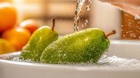 Fresh green pears being washed under running water in kitchen sink with water droplets, ideal for food preparation and healthy eating concepts.