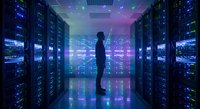 Silhouette of professional IT specialist standing in modern data center server room with glowing blue and purple neon lights creating futuristic atmosphere.