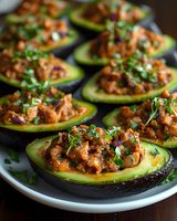 Stuffed avocado halves filled with savory meat mixture and fresh herbs on white plate. Healthy low-carb dinner recipe for keto diet and clean eating lifestyle.