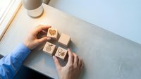 Hands arranging wooden blocks with business icons on desk surface for strategic planning and organization concepts.