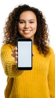 Young woman with curly brown hair and mixed ethnicity wearing yellow knit sweater holding smartphone with blank white screen for app mockup or advertisement placement.