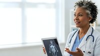 African American female doctor with stethoscope holding tablet displaying medical scan in bright hospital office for healthcare technology consultation.