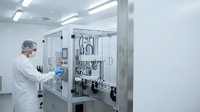 Pharmaceutical technician in white coat operating automated filling machine in sterile cleanroom facility for drug manufacturing and quality control.