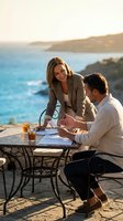 Professional businesswoman and businessman discussing documents at seaside cafe during golden hour with ocean view for corporate meetings and negotiations.