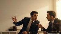 Two professional businessmen in suits having intense discussion during corporate meeting with dramatic lighting and serious expressions.