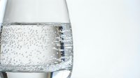 Sparkling water in a clear glass with bubbles rising, close-up shot on a light background, conveying freshness and hydration.