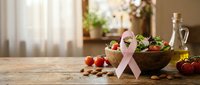 Pink ribbon breast cancer awareness symbol with fresh healthy vegetables and fruits on wooden kitchen counter promoting wellness and nutrition.