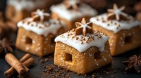 Mini gingerbread house cookies with white icing, star decorations and winter spices on dark background. Close up view of festive holiday baking treats.