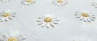 White daisy flowers embroidered on natural linen fabric texture creating delicate floral pattern for home decor and textile design projects.