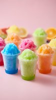 Colorful frozen slushie drinks in clear plastic cups with vibrant blue, green, and orange flavors on pink background. Summer beverage concept.