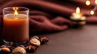 Warm autumn candle glowing with cozy blanket, walnuts and spices creating peaceful hygge atmosphere for relaxation and comfort at home.