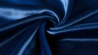 Luxurious navy blue silk fabric with elegant folds and soft sheen creates dramatic swirl pattern, highlighting rich texture and smooth surface for fashion and interior design.
