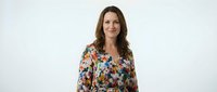 Woman with long brown hair and fair complexion wearing a colorful floral patterned shirt, smiling at camera against white background for portrait and professional use.