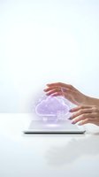 Hands protecting glowing purple cloud computing hologram above tablet on white desk representing data security and digital technology solutions.