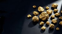 Golden nuggets scattered on dark surface with dramatic lighting creating shadows and highlights for luxury wealth concept.