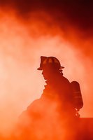 Silhouette of firefighter in protective gear against dramatic orange smoke background, representing emergency response and heroic service.