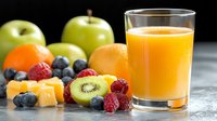 Fresh orange juice in glass with colorful fruits arrangement including kiwi, raspberries, blueberries, apples and cheese cubes on dark background, healthy breakfast concept.