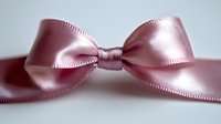 Elegant pink satin ribbon bow with delicate stitched edges on white background, macro close-up view showing luxurious fabric texture and soft sheen.