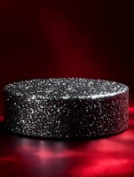 Black glittery round platform on dark red background with dramatic lighting and sparkly surface texture creates luxurious product display setting.