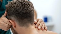 Caucasian man receiving professional neck massage therapy in medical office, close-up view of hands massaging upper spine and base of skull for pain relief.