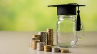 Education savings fund concept with graduation cap on glass jar and stacked coins representing tuition costs and financial planning for college.